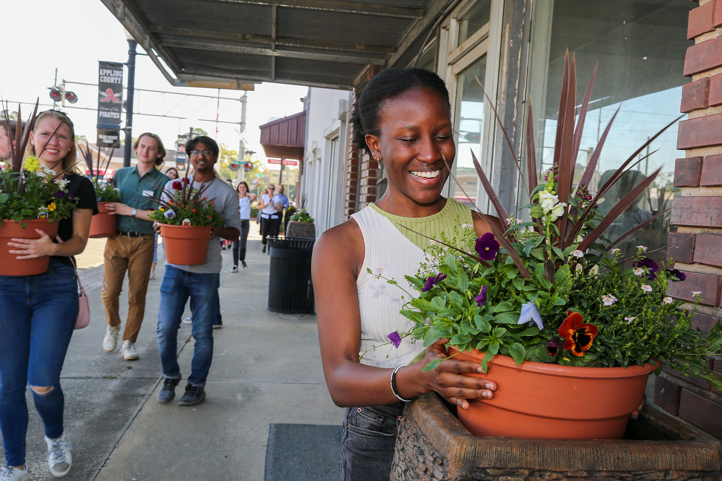 student places plant in planter in downtown Baxley