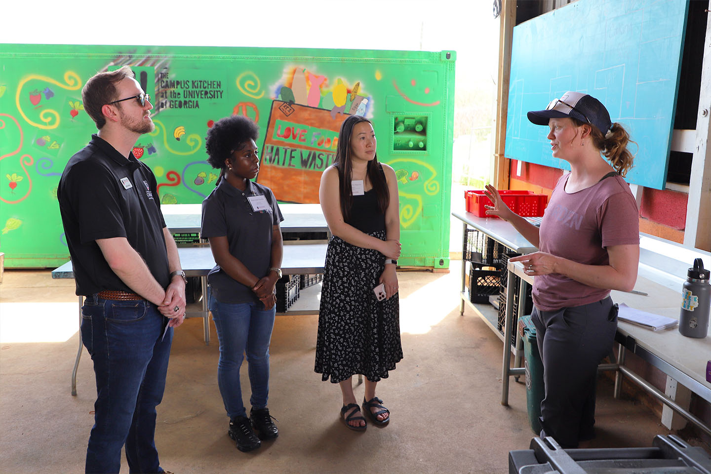 one person presents to three other people with signs saying Campus Kitchen in the background