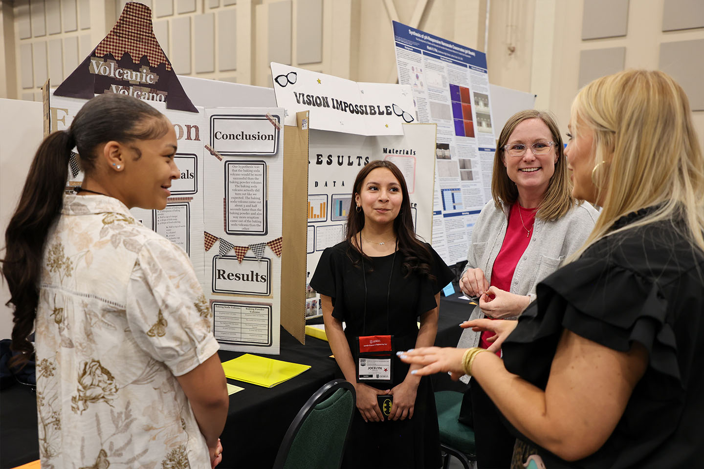 two students talk to their teacher in front of their project at the Georgia Science and Engineering Fair.