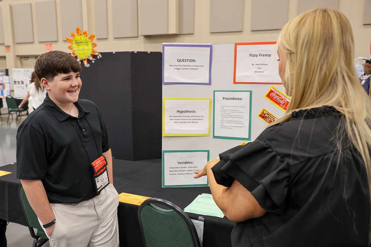 Middle school student talks with his teacher in front of his project.