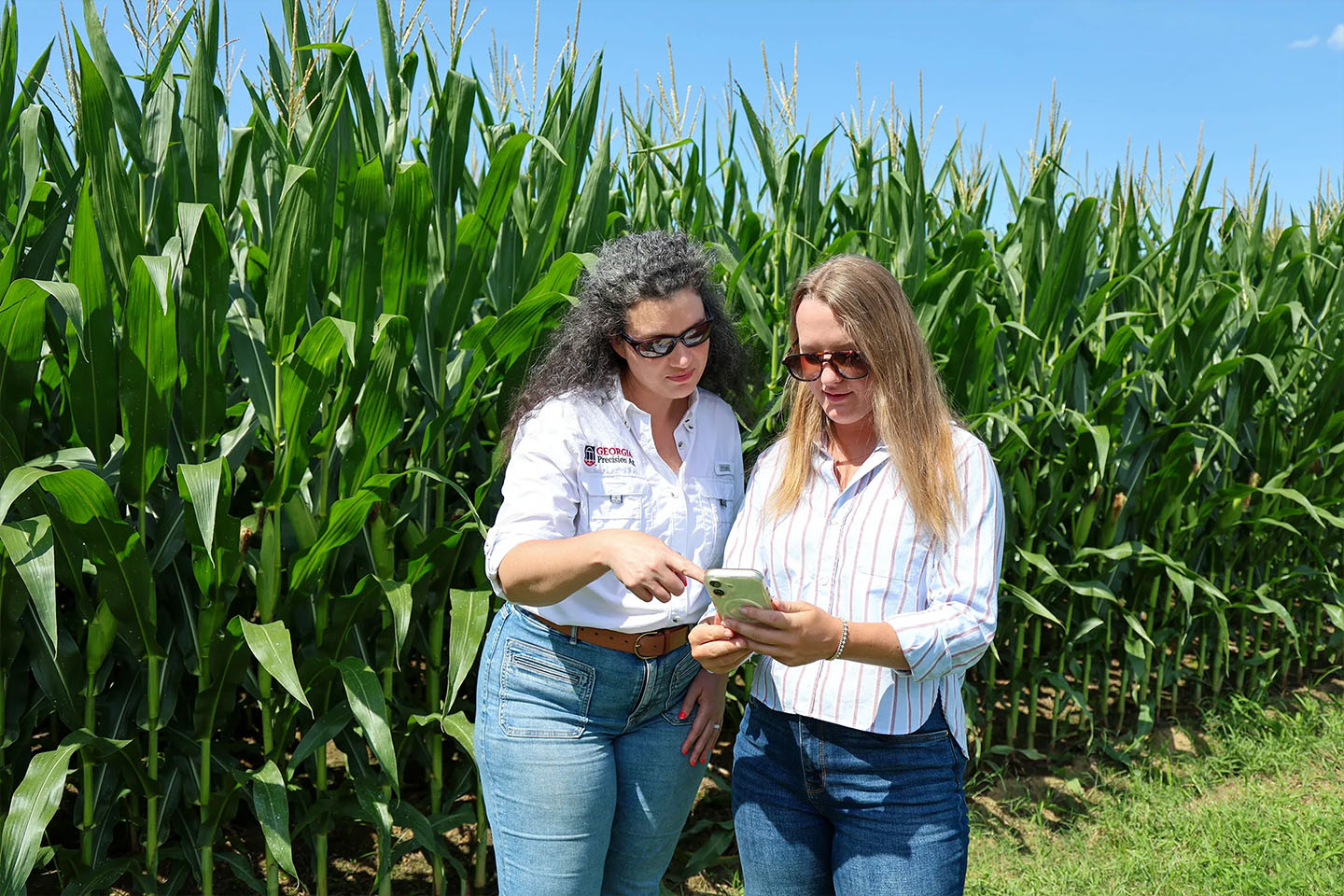 two women look at a phone in a corn field