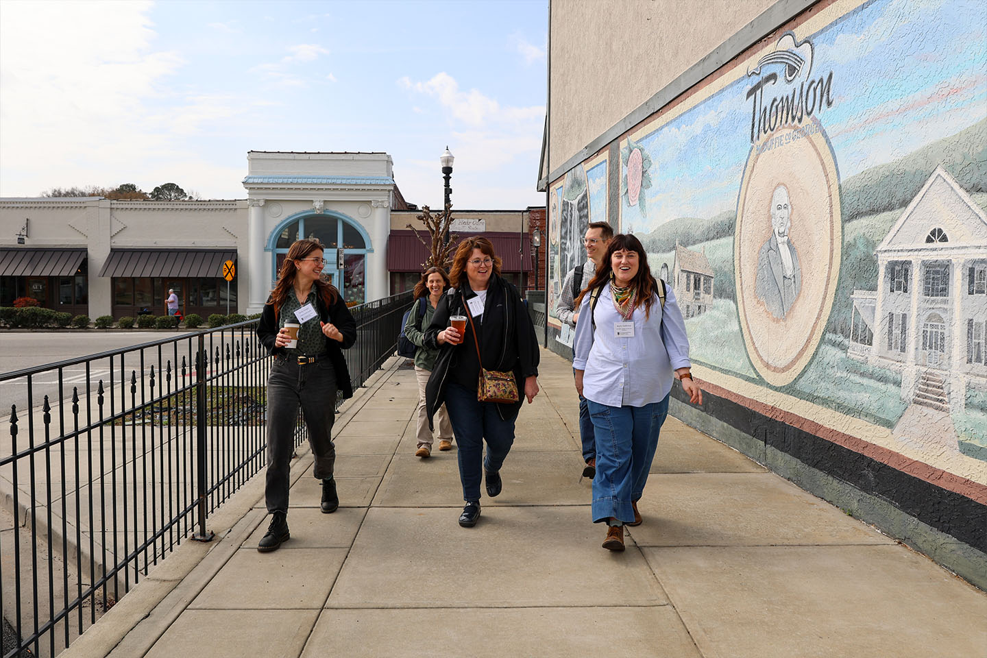 5 faculty members walking in downtown thomson by a mural