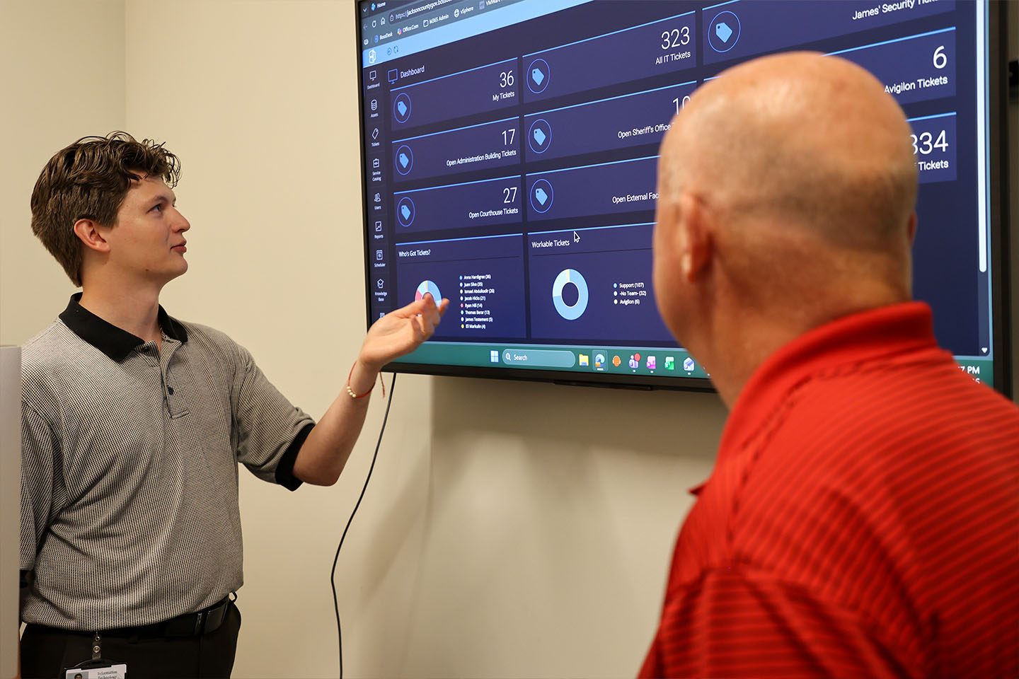 Christopher points to a large presentation screen while presenting to Barry.